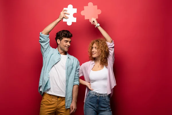 Felice coppia che tiene pezzi di puzzle, isolato sul rosso — Foto stock