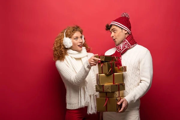 Heureux couple en tenue d'hiver tenant cadeaux de Noël sur rouge — Photo de stock