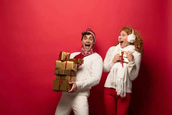 Pareja emocionada en traje de invierno celebración de regalos de Navidad en rojo - foto de stock