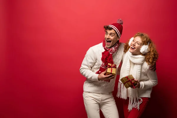 Hermosa pareja feliz en traje de invierno celebración de regalos de Navidad aislados en rojo - foto de stock