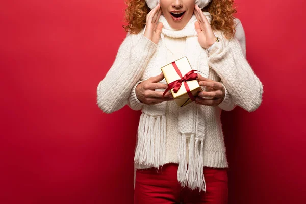 Abgeschnittene Ansicht von überraschter Frau und Mann im Winteroutfit mit Weihnachtsgeschenk isoliert auf Rot — Stockfoto