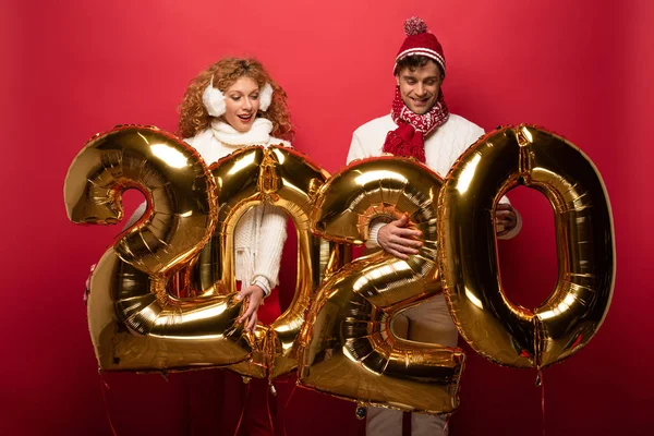 Glückliches Paar im Winteroutfit mit goldenen Luftballons auf rotem Grund — Stockfoto