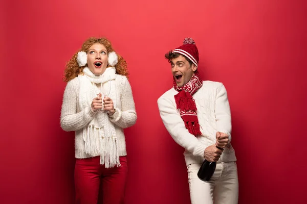 Pareja emocionada en traje de invierno celebración de champán para celebrar la Navidad, en rojo - foto de stock