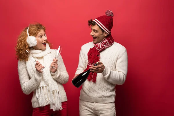 Beau couple heureux en tenue d'hiver tenant champagne pour célébrer Noël, sur rouge — Photo de stock