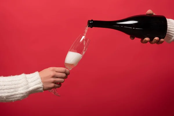 Обрізаний вид людини, що висипає шампанське з пляшки в окуляри, ізольовані на червоному — стокове фото