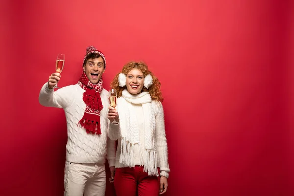 Coppia felice in abito invernale brindare con bicchieri di champagne, isolato su rosso — Foto stock