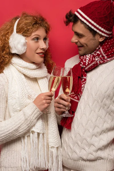 Beautiful man and woman in winter outfit clinking with champagne glasses, isolated on red — Stock Photo