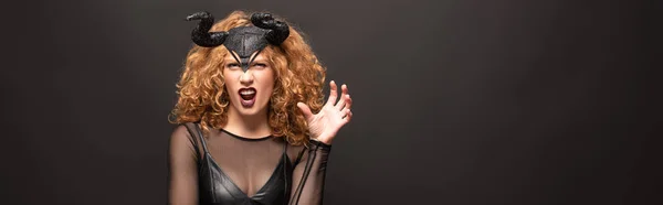 Scary redhead woman gesturing in halloween costume with horns on black — Stock Photo