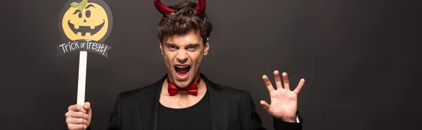 Brunetta uomo in costume diavolo con zucca dolcetto o trattare segno di Halloween su nero — Foto stock