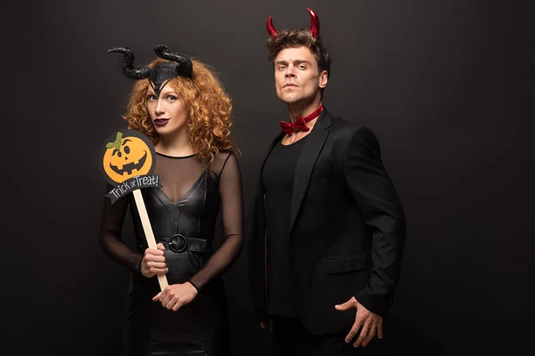 Joven pareja posando en halloween trajes con calabaza truco o tratar signo en negro - foto de stock