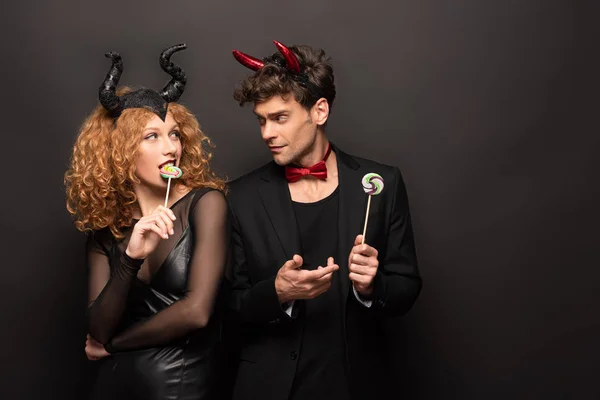 Hermosa pareja en halloween trajes celebración piruletas en negro - foto de stock