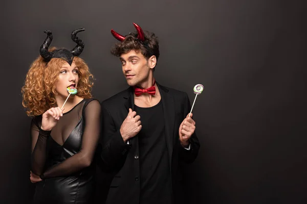 Hermosa pareja posando en trajes de halloween con piruletas dulces en negro - foto de stock