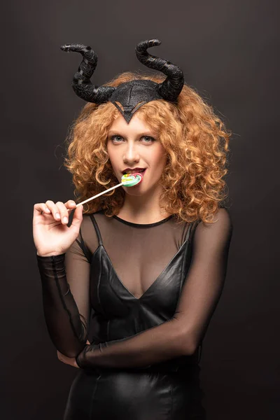 Schöne sexy Frau im bösartigen Kostüm isst Lutscher auf halloween auf schwarz — Stockfoto