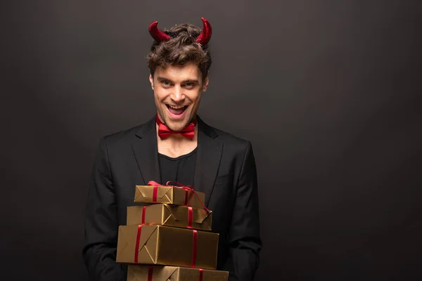 Homme gai en costume diable sur Halloween tenant des cadeaux sur noir — Photo de stock