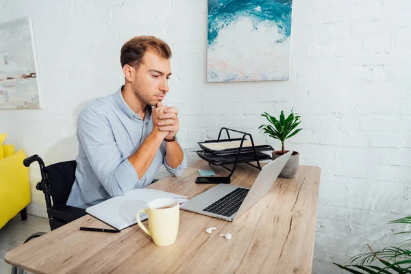 Mann im Rollstuhl schaut am Arbeitsplatz auf Laptop — Stockfoto