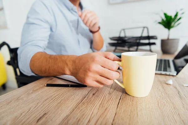 Cropped view of man in wheelchair drinking coffee at office desk — Stock Photo