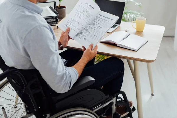 Ausgeschnittene Ansicht eines Mannes im Rollstuhl beim Betrachten von Papieren am Arbeitsplatz — Stockfoto