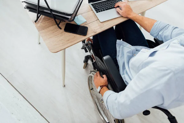 Vista recortada del hombre en silla de ruedas usando portátil en el lugar de trabajo - foto de stock