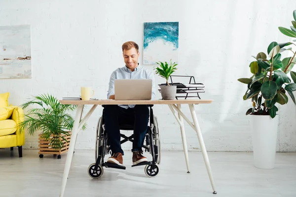 Freelance souriant en fauteuil roulant en utilisant un ordinateur portable au bureau dans le salon — Photo de stock