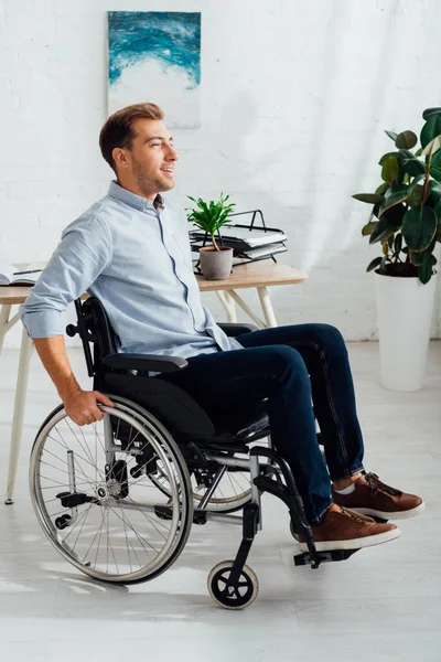 Hombre sonriente en silla de ruedas y mirando hacia otro lado en el salón - foto de stock