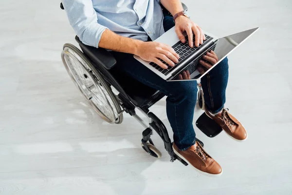 Обрезанный вид человека, сидящего в инвалидной коляске и использующего ноутбук — стоковое фото