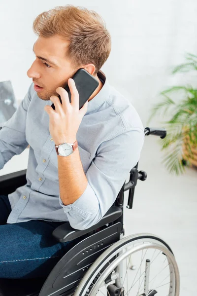 Vista lateral del hombre en silla de ruedas hablando en smartphone - foto de stock