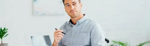 Hombre pensativo sosteniendo la pluma y mirando hacia otro lado en la sala de estar, plano panorámico - foto de stock