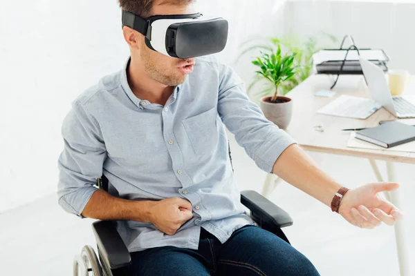 Homem excitado em cadeira de rodas usando headset realidade virtual por local de trabalho — Fotografia de Stock