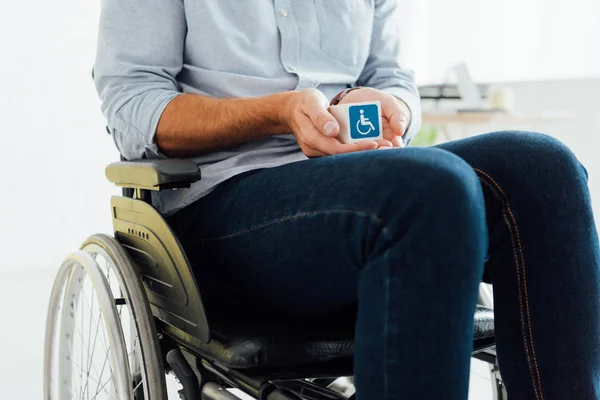 Обрезанный вид человека в инвалидной коляске, держащего куб с табличкой инвалида — стоковое фото