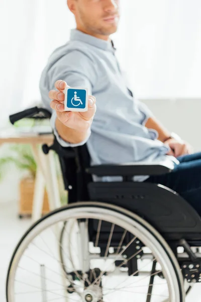 Vista recortada del hombre en silla de ruedas que muestra el cubo con signo de discapacidad - foto de stock