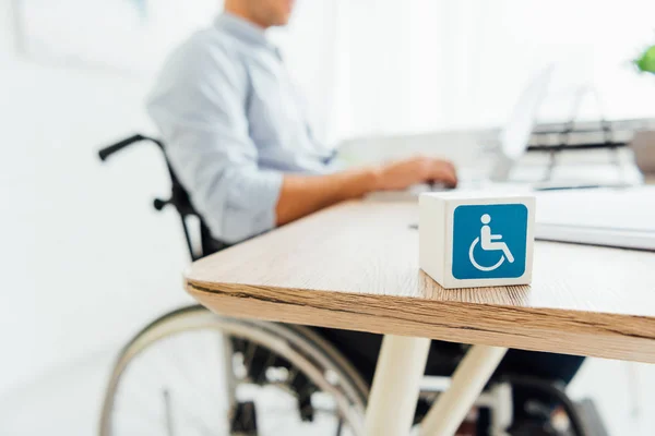 Selective focus of cube with disabled sign and man in wheelchair sitting at table — Stock Photo