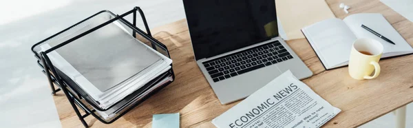 Panoramic shot of laptop with blank screen, cup of tea and newspaper on table — Stock Photo