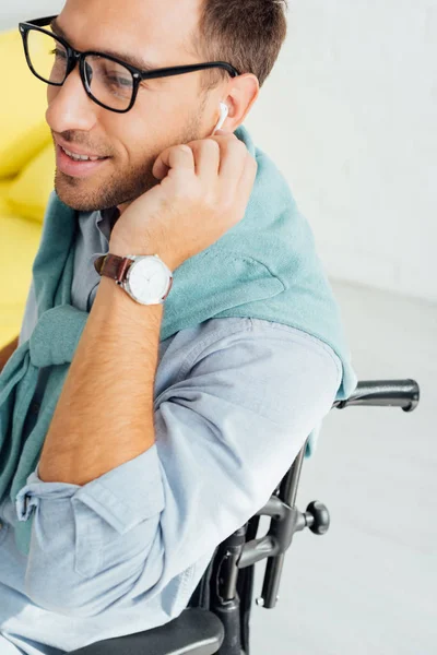 Hombre sonriente en silla de ruedas usando auriculares inalámbricos - foto de stock