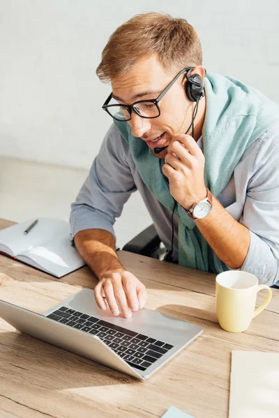 Call center operator in headset using laptop at desk — Stock Photo