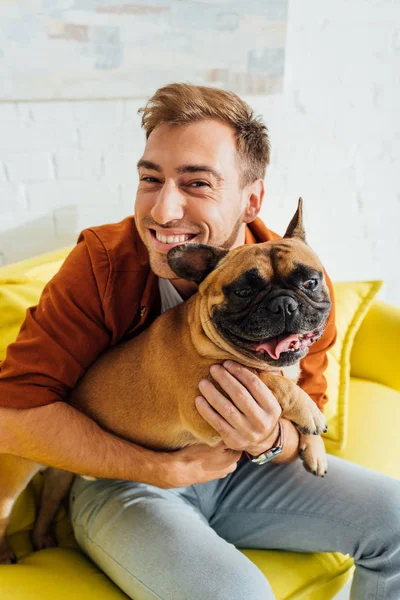 Homme souriant regardant la caméra et étreignant bouledogue français — Photo de stock