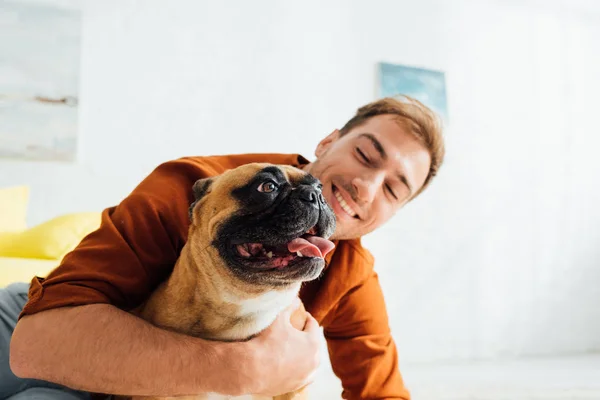 Glücklicher Mann umarmt französische Bulldogge im Wohnzimmer — Stockfoto