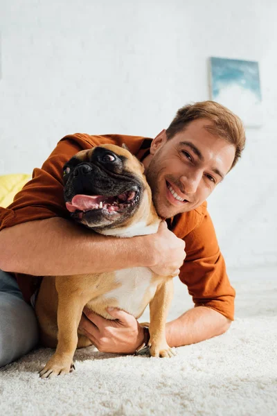 Hombre abrazando bulldog francés y sonriendo a la cámara - foto de stock