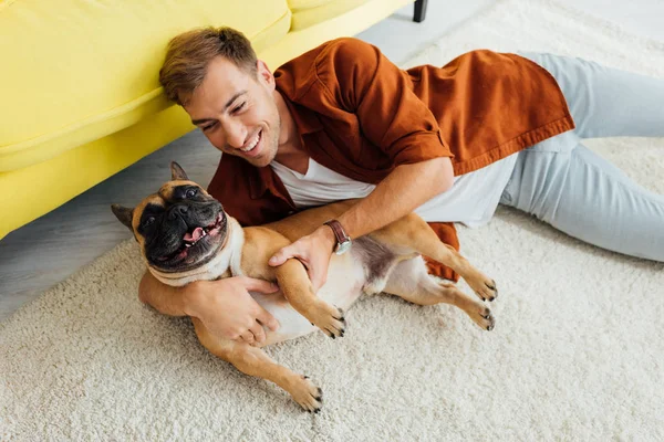 Homme souriant couché avec un bouledogue français sur le sol par un canapé — Photo de stock