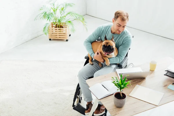 Hombre discapacitado sosteniendo bulldog francés y mirando el ordenador portátil en la sala de estar - foto de stock