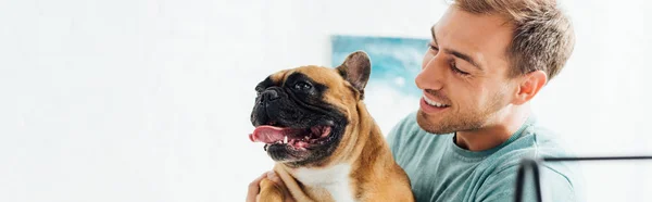Panorâmica tiro de homem sorridente segurando bulldog francês — Fotografia de Stock