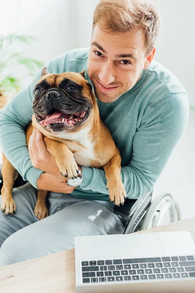 Hombre discapacitado sosteniendo bulldog francés y sonriendo a la cámara - foto de stock