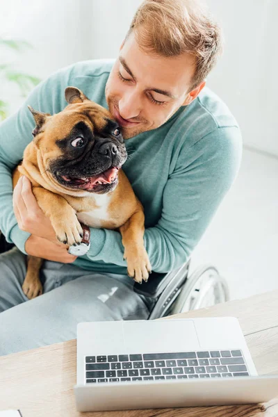 Smiling man hugging french bulldog while working on laptop — Stock Photo