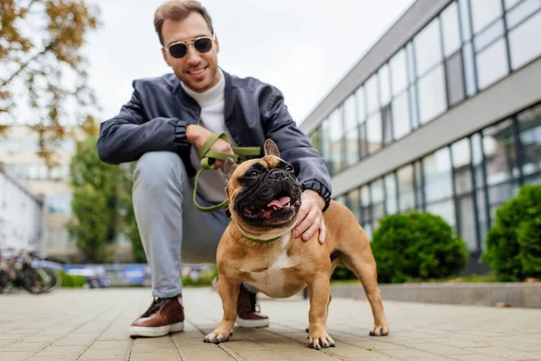 Улыбающийся мужчина держит в руках поводок и ласкает собаку на городской улице — стоковое фото