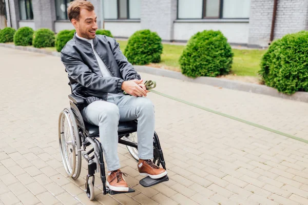 Sorridente uomo disabile tenendo il guinzaglio e guardando lateralmente la strada urbana — Foto stock