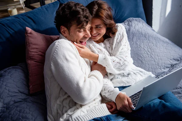 High angle view of smiling girlfriend with laptop tickling handsome boyfriend — Stock Photo