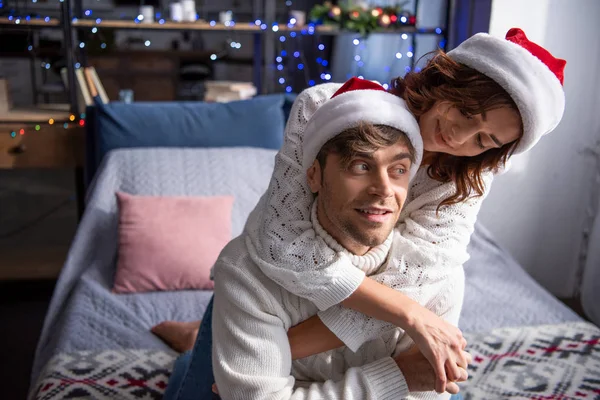 Petite amie souriante étreignant petit ami dans le chapeau de Père Noël au moment de Noël — Photo de stock