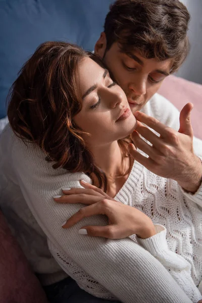 Vue grand angle de beau copain étreignant et touchant visage de petite amie en pull avec les yeux fermés — Photo de stock