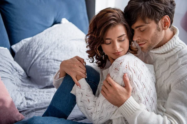 Guapo novio abrazando novia en suéter con los ojos cerrados - foto de stock