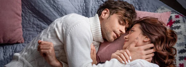 Colpo panoramico di fidanzato e fidanzata in maglioni abbracciati e sdraiati a letto — Foto stock