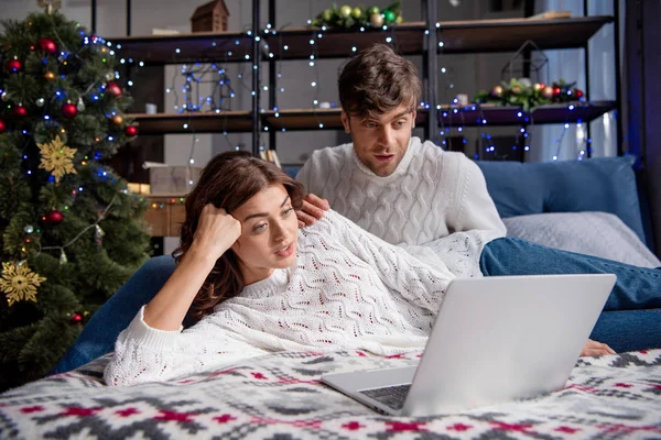 Шокований хлопець і дівчина в светрах дивиться на ноутбук в різдвяний час — стокове фото